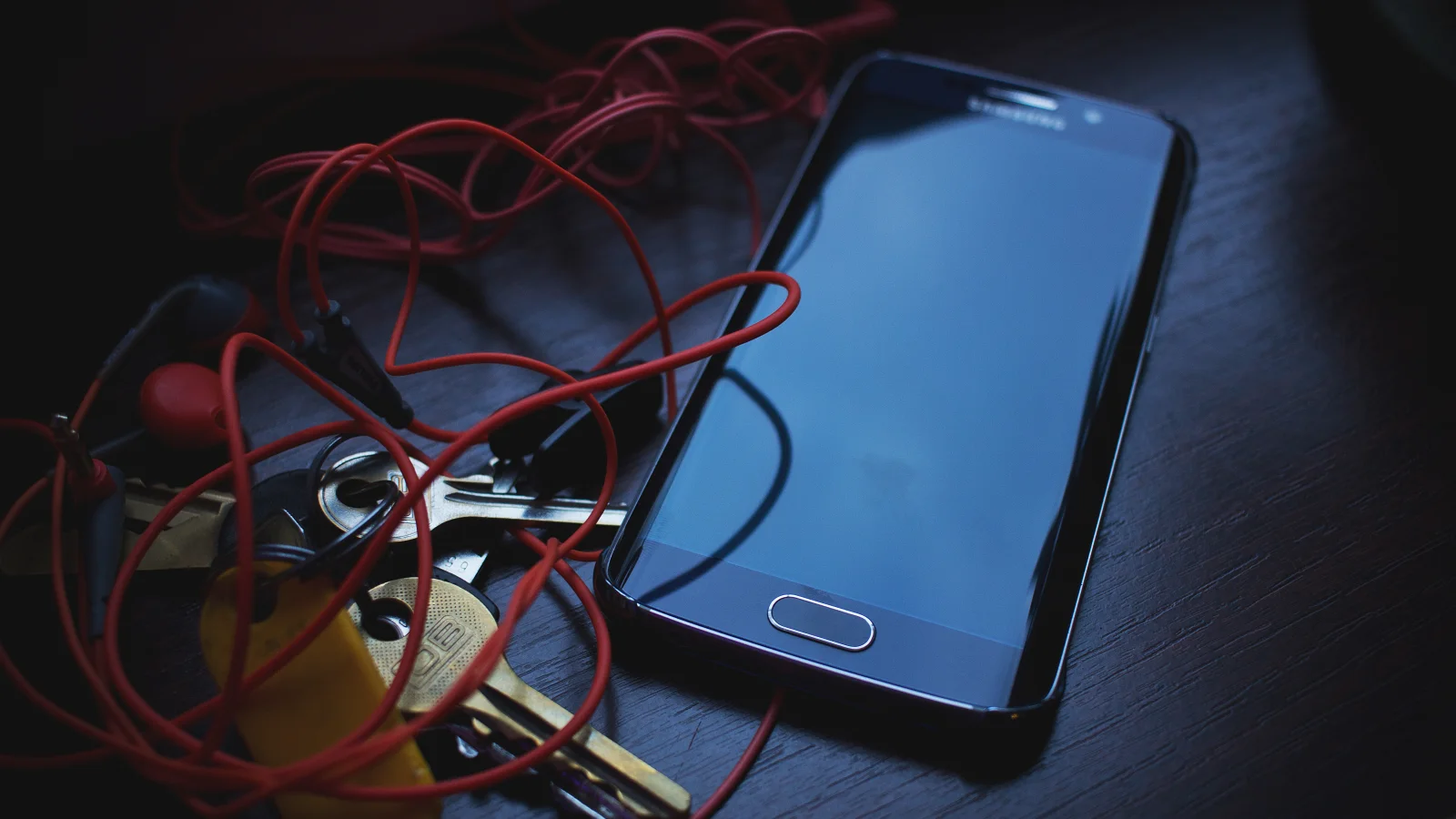 Smartphone, headphones and car keys arranged on a wooden table while booking information is checked