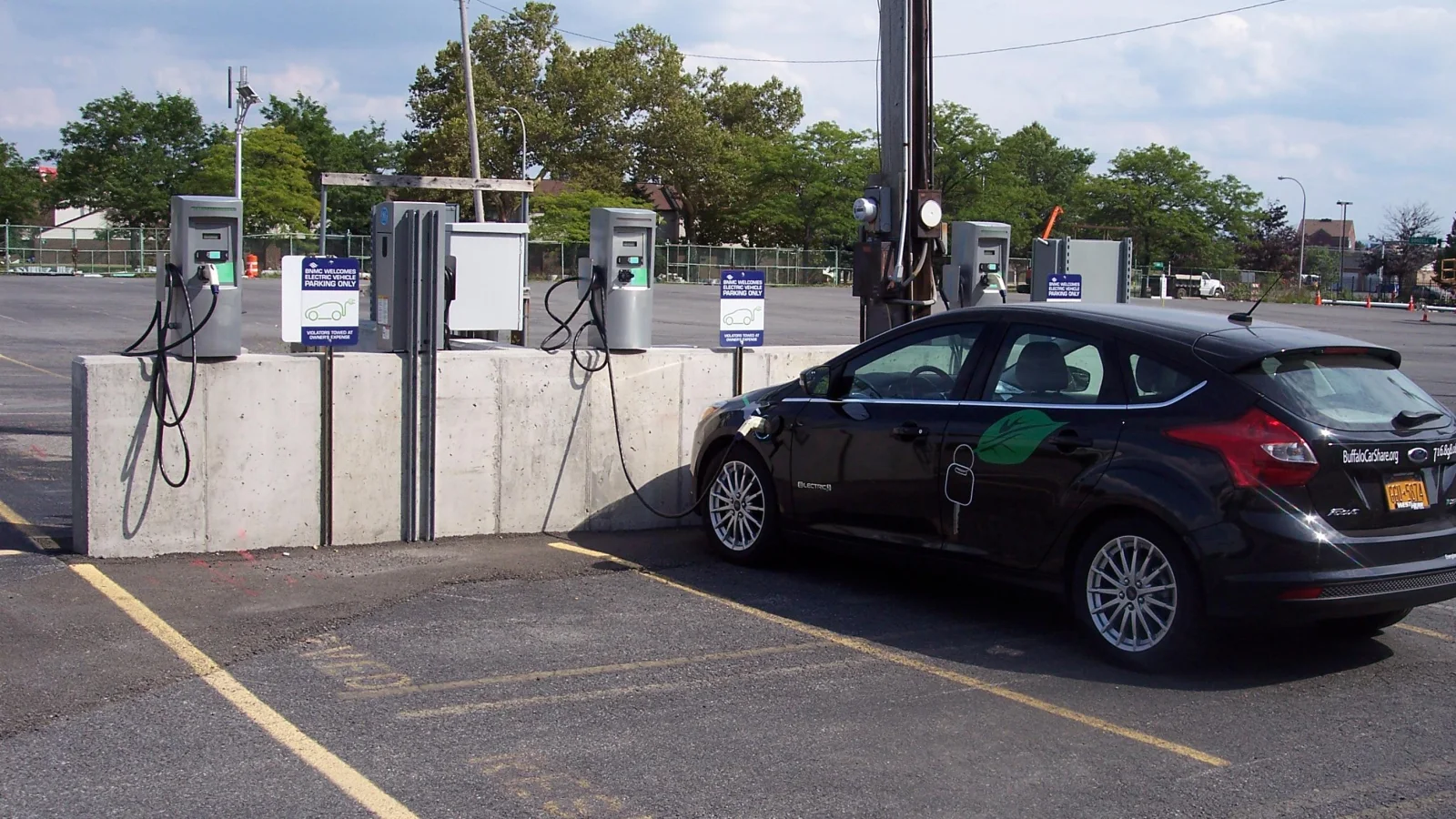 A black electric car connected to a public charging station in daylight